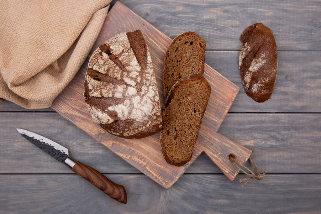 Pan de centeno pan redondo cortado en trozos en una tabla de madera con un cuchillo de madera rústica. Vista superior. - Foto, imagen