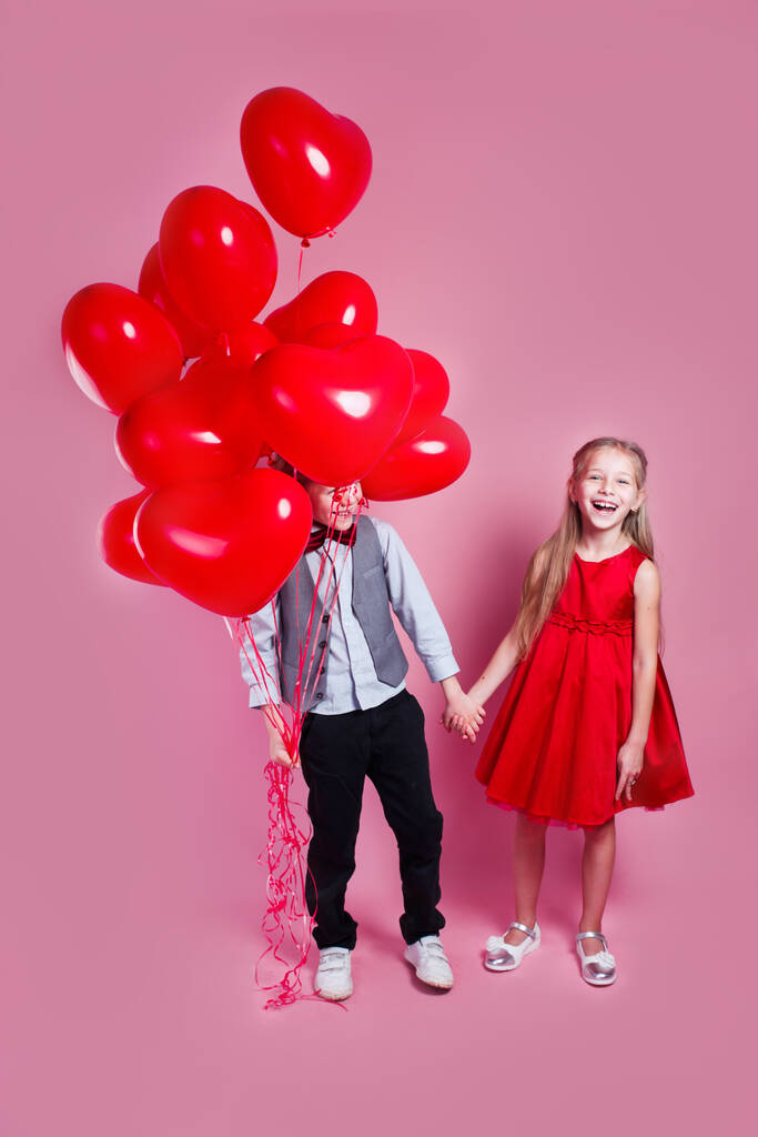 Dia dos Namorados. Duas crianças felizes com balões de ar em forma de coração no fundo rosa. Primeiro amor - Foto, Imagem