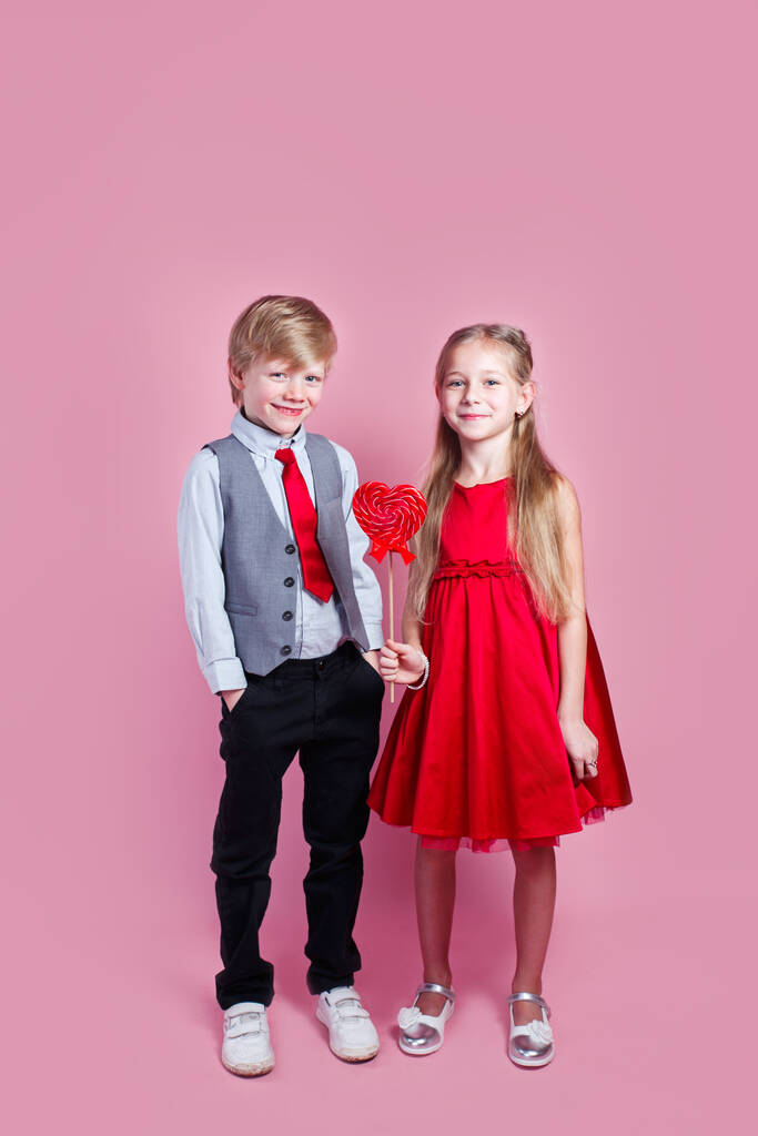 Valentine's day concept. Funny boy and little girl with candy red lollipop in heart shape. Beautiful children eat sweets. - Photo, Image