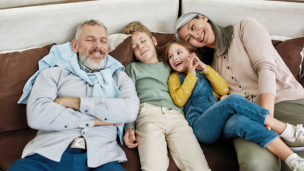 Portrait de grands-parents et petits-enfants heureux couchés ensemble sur le canapé dans le salon, relaxant et souriant à la caméra - Photo, image