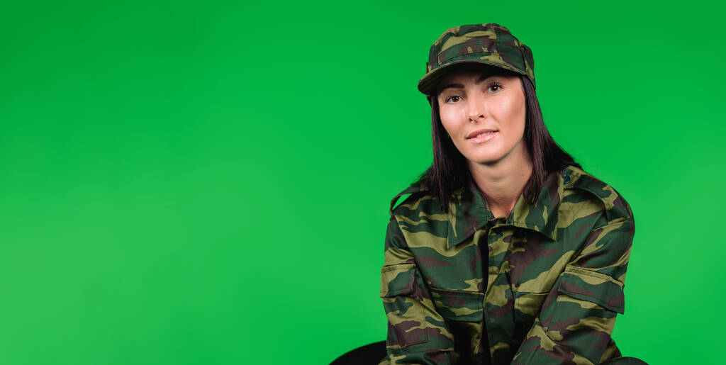 Banner- formato longo. Retrato de uma mulher bonita em uniforme militar olhando para a câmera em um fundo verde com espaço lateral em branco. - Foto, Imagem