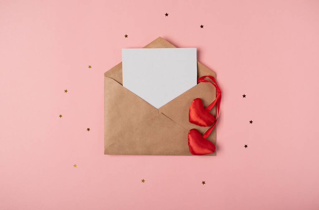 バラの背景に内側と赤の心の中に紙の空白のシートでクラフト封筒。バレンタインデーのコンセプトのためのロマンチックな愛の手紙。テキストのスペース. - 写真・画像