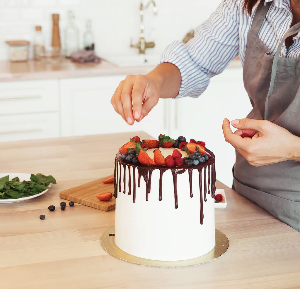 Estilo de vida, pessoas, cozinhar e conceito freelancer: fechar as mãos femininas decorar o bolo com chocolate e bagas - Foto, Imagem