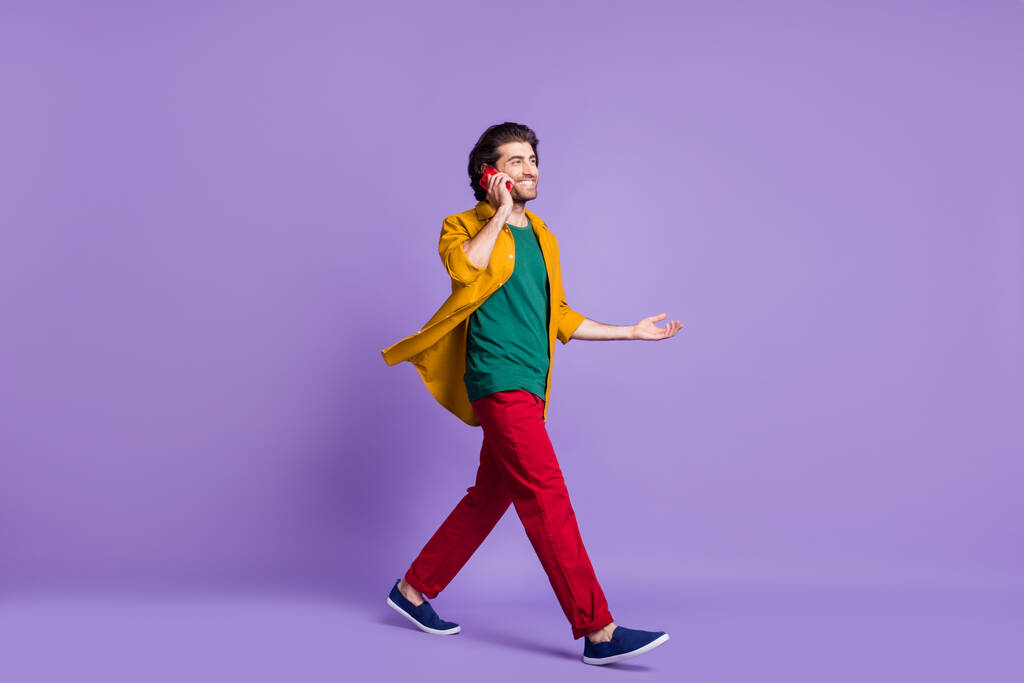 Täyspitkä kuva muotokuva mies puhuu puhelimessa kävely eristetty eloisa violetti värillinen tausta - Valokuva, kuva