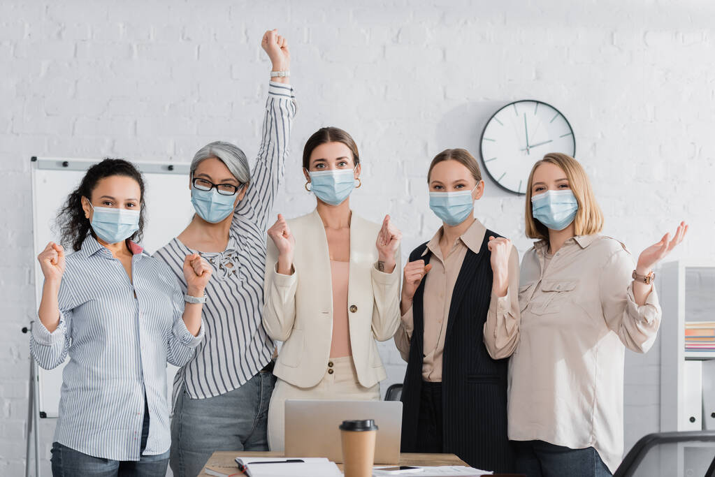 ενθουσιασμένοι πολυπολιτισμικές επιχειρηματίες σε ιατρικές μάσκες κοντά στο γραφείο - Φωτογραφία, εικόνα