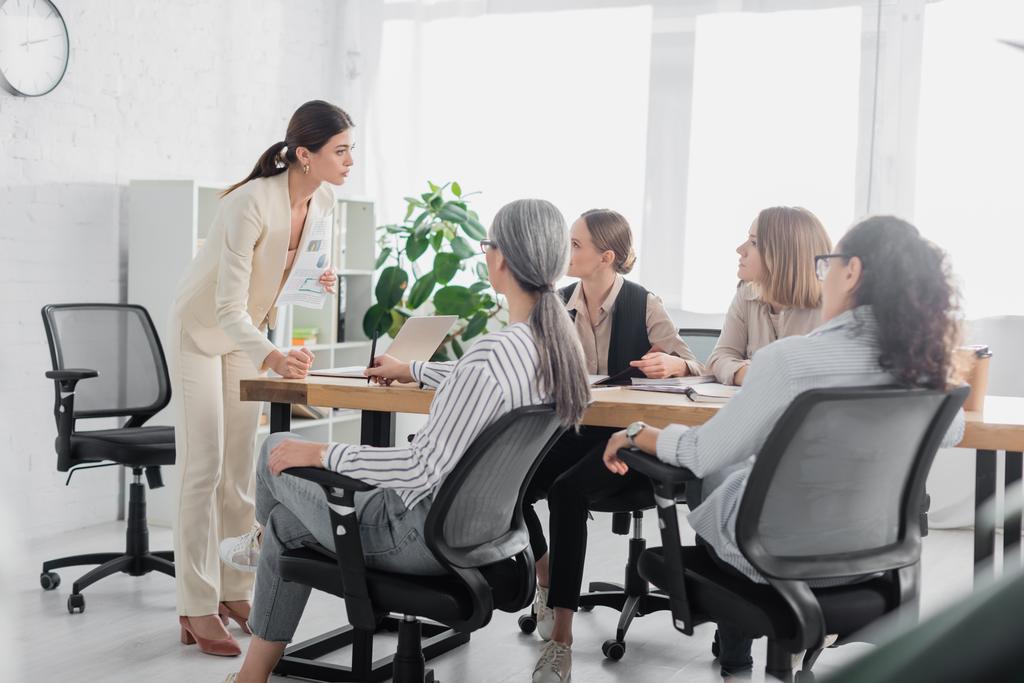 veeleisende teamleider staat bij multiculturele zakenvrouwen tijdens bijeenkomst in functie  - Foto, afbeelding