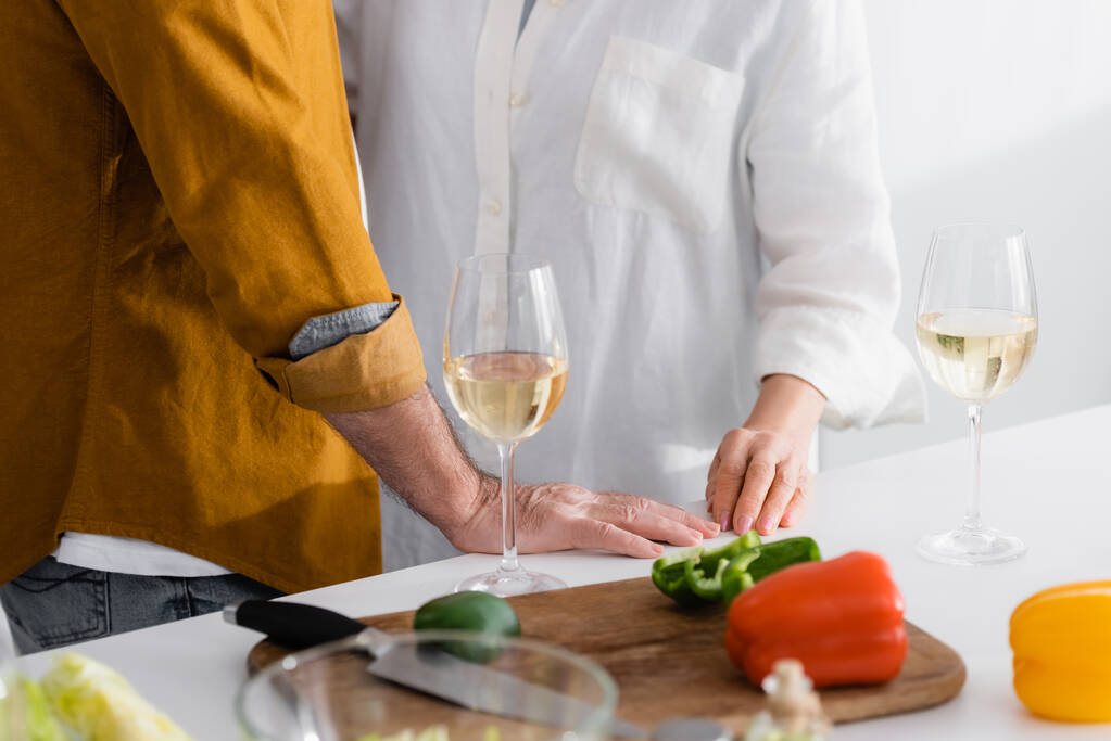 Обрезанный вид пожилой пары, стоящей рядом со стаканами с вином и паприкой на кухонном столе  - Фото, изображение