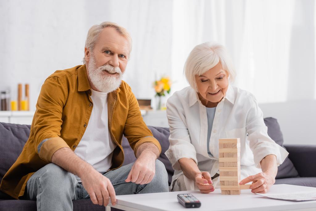 Lächelndes Senioren-Paar spielt Holzturmspiel auf Couchtisch  - Foto, Bild