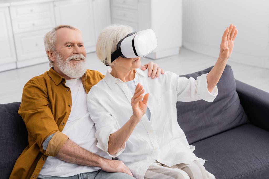 Senior man embracing wife in vr headset on sofa  - Photo, Image