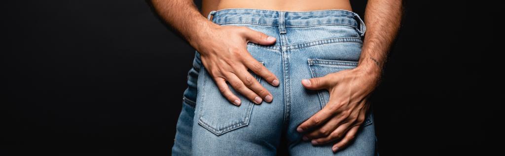 黒のバナーに隔離された尻を抱く男の近くのジーンズの女性のクロップドビュー - 写真・画像