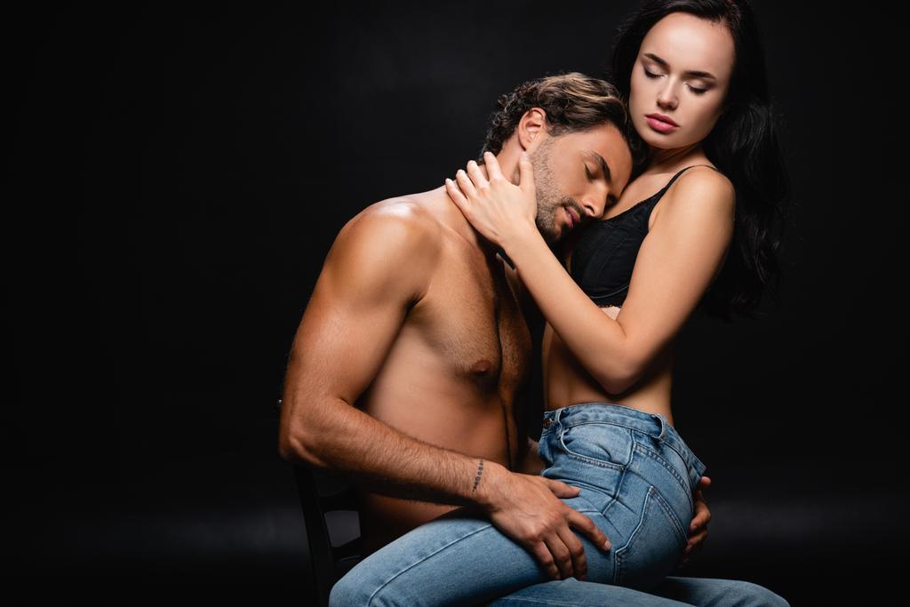 passionate young couple in jeans hugging with closed eyes on chair on black - Photo, Image