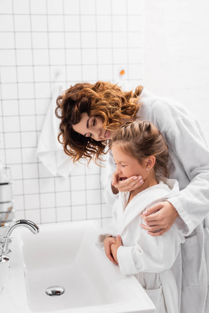 Gülümseyen kadın modern banyoda lavabonun yanında çocuğa sarılıyor.  - Fotoğraf, Görsel