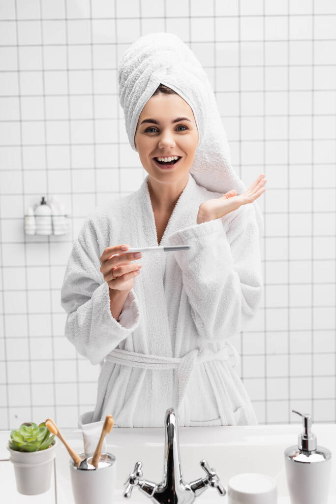 Веселая женщина в халате проводит тест на беременность в ванной комнате  - Фото, изображение
