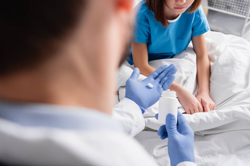 Ausgeschnittene Ansicht eines Arztes, der einem kranken Mädchen im Krankenhaus eine Pille verabreicht, verschwommener Vordergrund - Foto, Bild