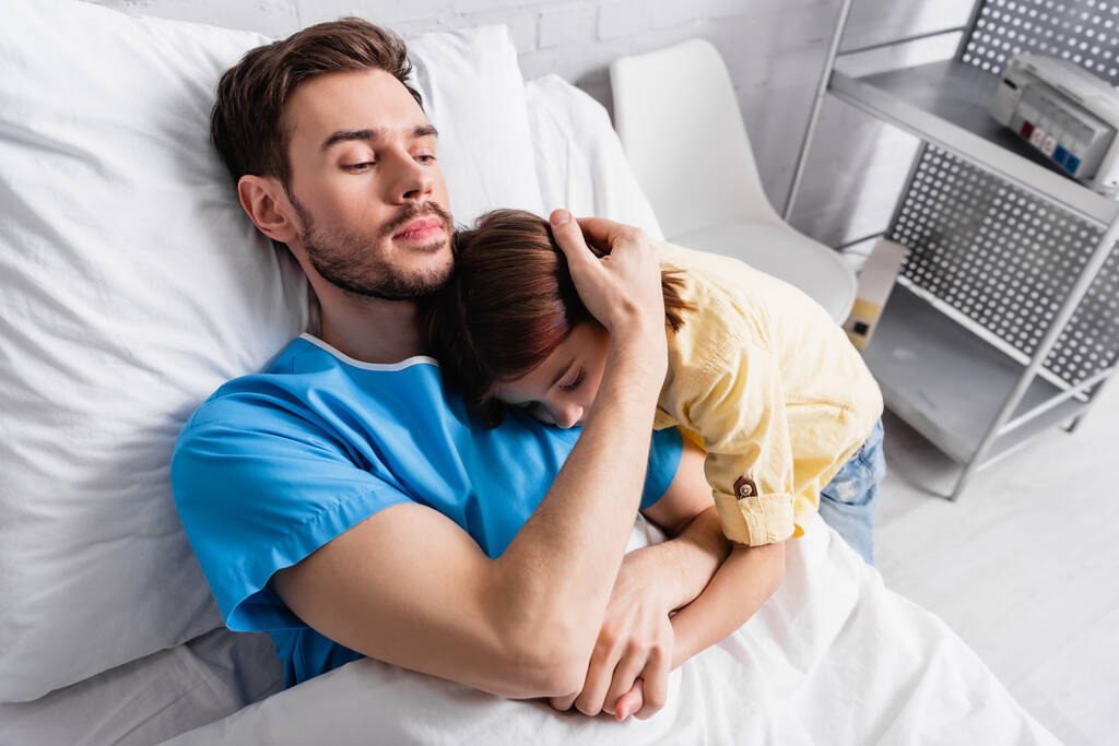 chory człowiek obejmujący córkę leżącą w szpitalnym łóżku - Zdjęcie, obraz