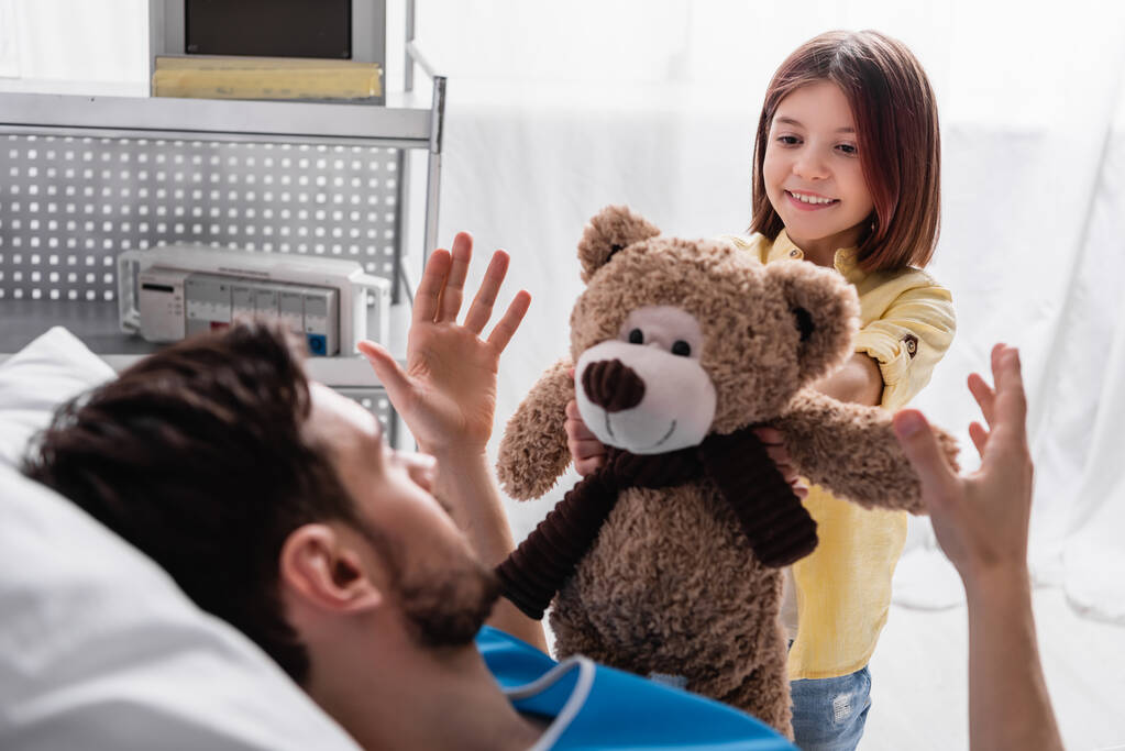 fille souriante donnant ours en peluche au père couché à l'hôpital - Photo, image