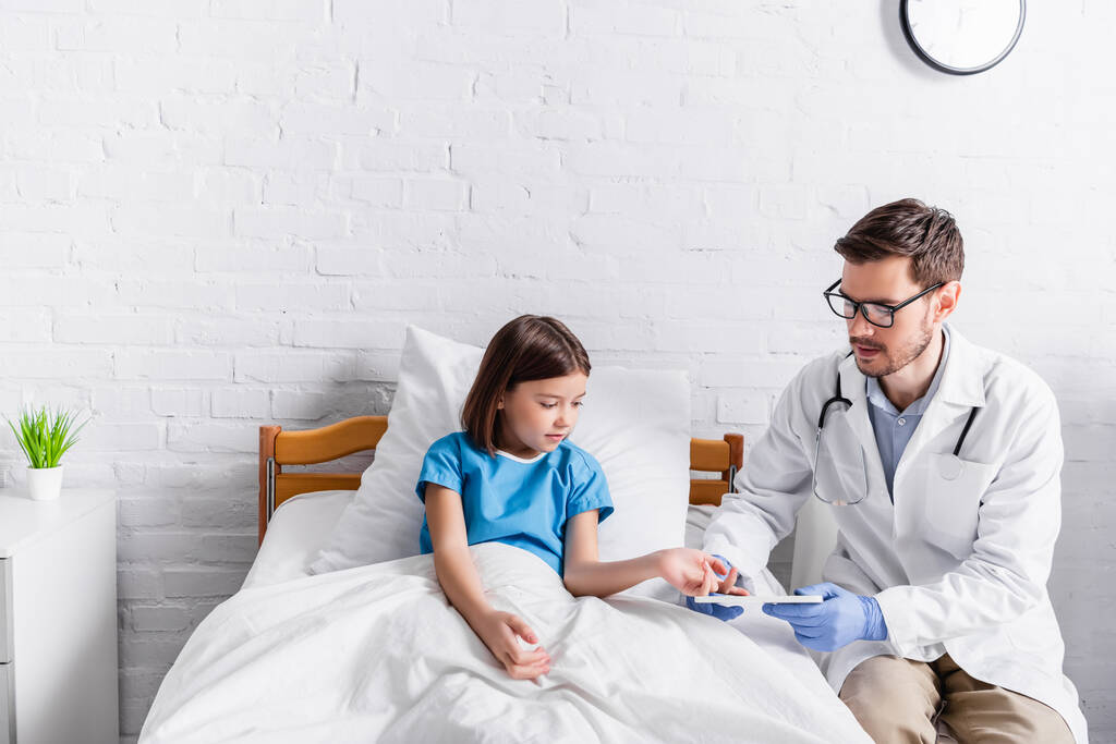 хвора дитина вказує на цифровий планшет в руках лікаря в лікарні
 - Фото, зображення