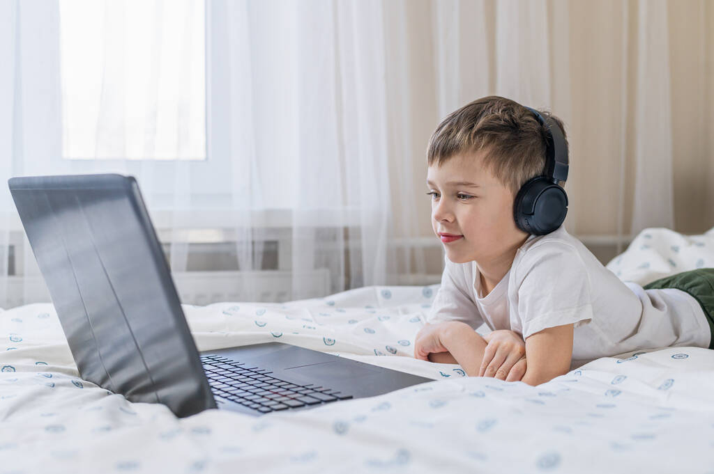 Menino com fones de ouvido está assistindo a um vídeo em um laptop. - Foto, Imagem