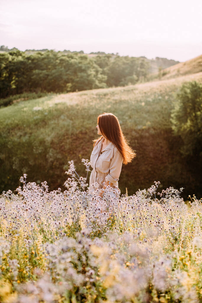 meisje op het grasveld bloemen zomer landschap zonsondergang licht - Foto, afbeelding
