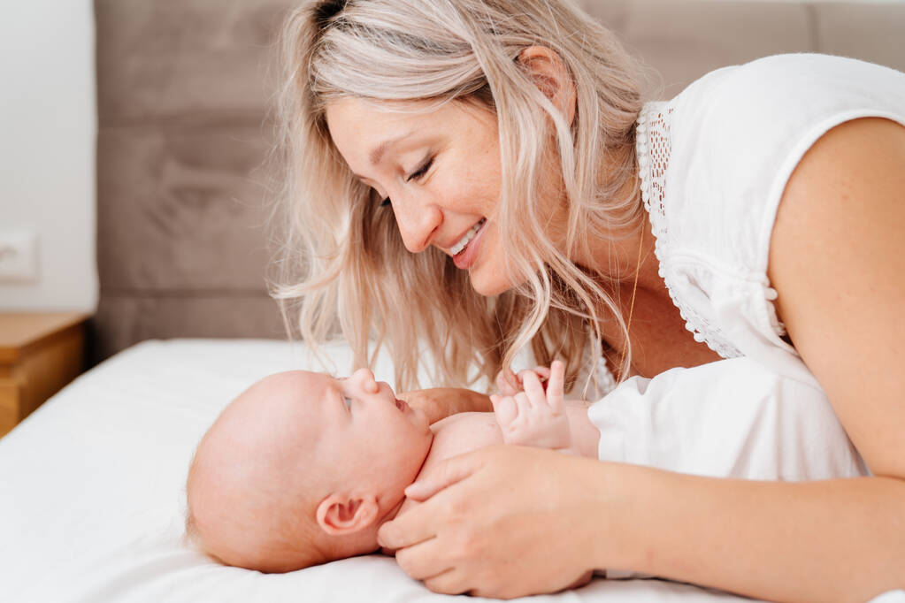 Anne, anne sütü içtikten sonra bembeyaz bir yatakta bir bebekle yatıyor..  - Fotoğraf, Görsel