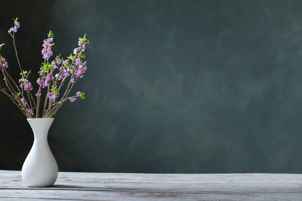квіти дафни у вазі на старому дерев'яному столі на фоні зеленої стіни
 - Фото, зображення