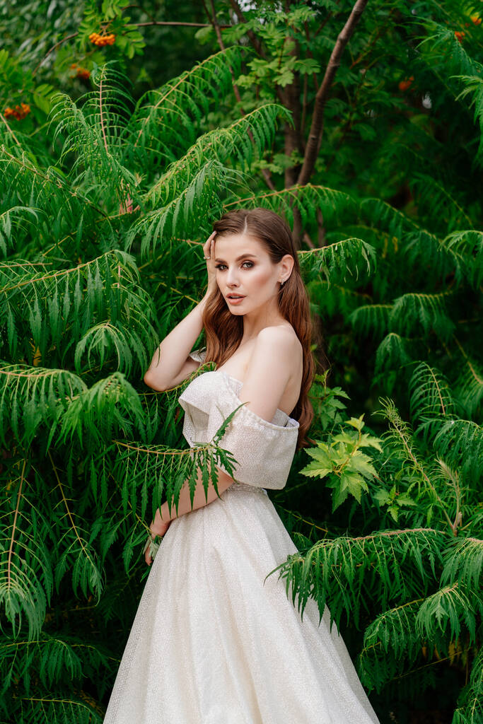 緑の葉にポーズをとった白いドレスを着た美しい女性. - 写真・画像