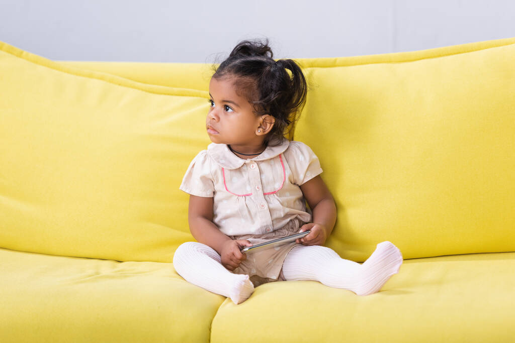 toddler african american child holding smartphone while sitting on sofa - Photo, Image