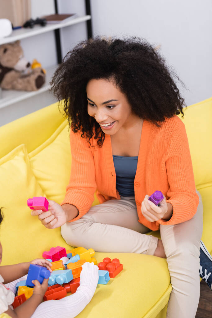 feliz afro-americana mãe jogando blocos de construção com a filha da criança no sofá - Foto, Imagem