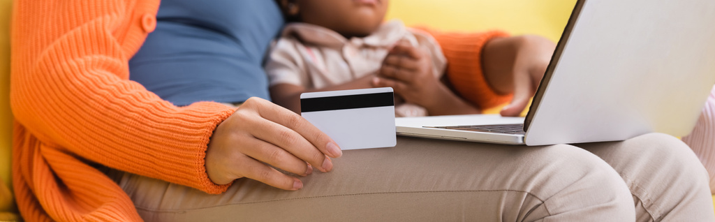 visão parcial da mãe afro-americana segurando cartão de crédito e usando laptop perto da filha da criança, banner - Foto, Imagem