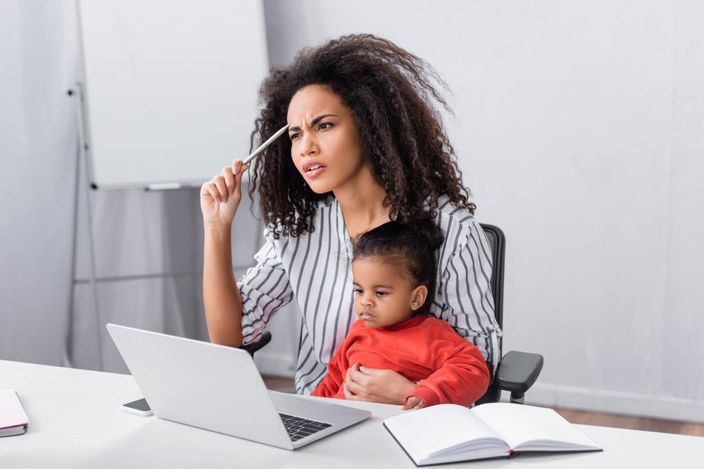 pensativo africano americano madre sentado con niño hija mientras trabajo desde casa  - Foto, imagen
