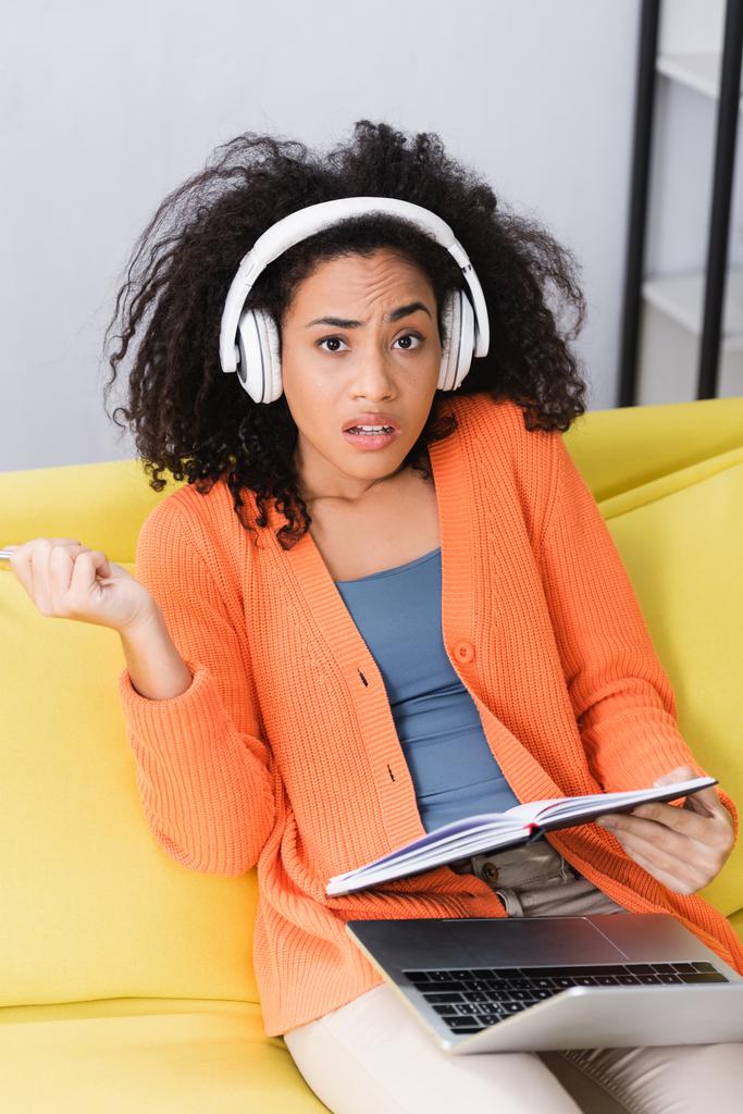 afro-americana segurando notebook e ouvindo podcast em fones de ouvido - Foto, Imagem