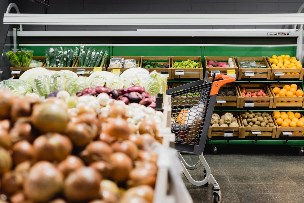 Τρόλεϊ αγορών κοντά λαχανικά σε θολή πρώτο πλάνο στο σούπερ μάρκετ  - Φωτογραφία, εικόνα