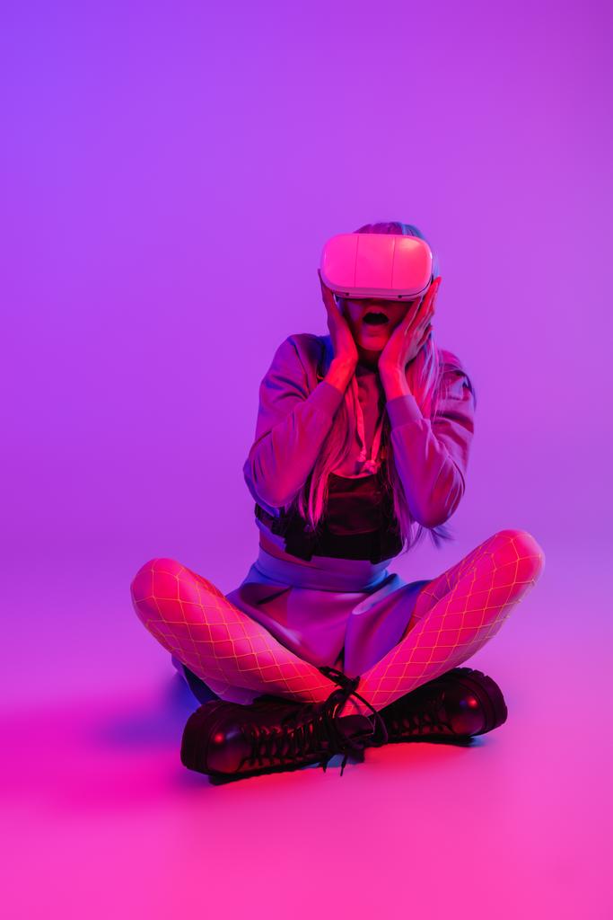 täyspitkä peloissaan nainen virtuaalitodellisuus kuulokkeet istuu violetti tausta  - Valokuva, kuva