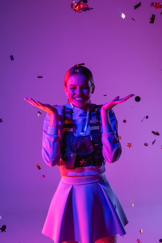 mujer alegre en traje elegante cerca de caer confeti en púrpura - Foto, imagen