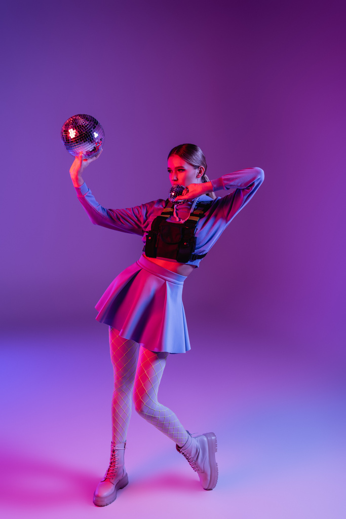 full length of trendy woman in skirt holding disco balls on purple - Photo, Image