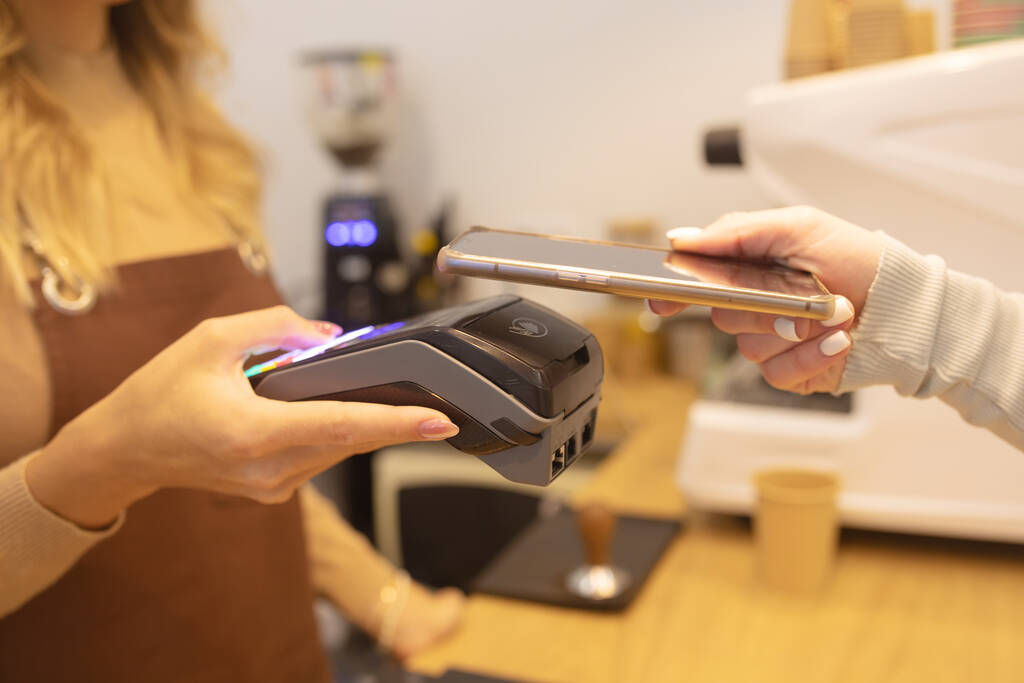 Περικοπή Shot της γυναίκας κρατώντας Smartphone με την τεχνολογία πληρωμής Χρησιμοποιώντας για την πληρωμή για Take Away Coffee σε ένα καφέ. - Φωτογραφία, εικόνα