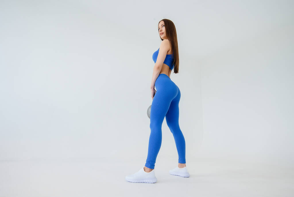 セクシーな若い女の子は白い背景に青いトラックスーツで体重で演習を実行します.フィットネス,健康的なライフスタイル - 写真・画像