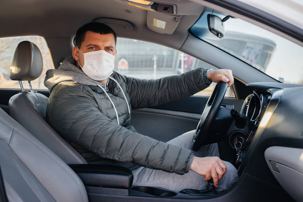 Salgın ve koronavirüs sırasında araba kullanırken maske takan genç bir adam direksiyonda oturuyor. Salgın - Fotoğraf, Görsel
