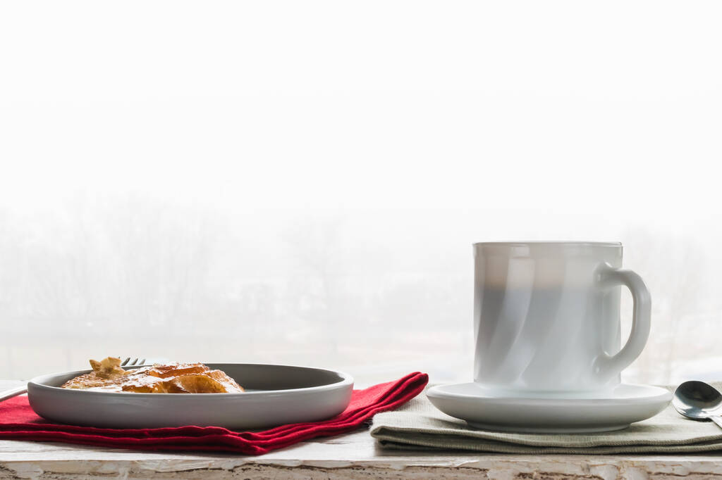 Una taza de café y un plato de panqueques sobre una mesa decorativa, sobre el fondo de la ventana - Foto, imagen