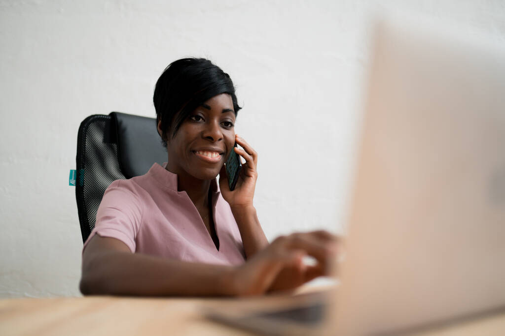 Une femme s'assoit à une table et regarde un ordinateur en passant un coup de fil. Travailler à distance - Photo, image