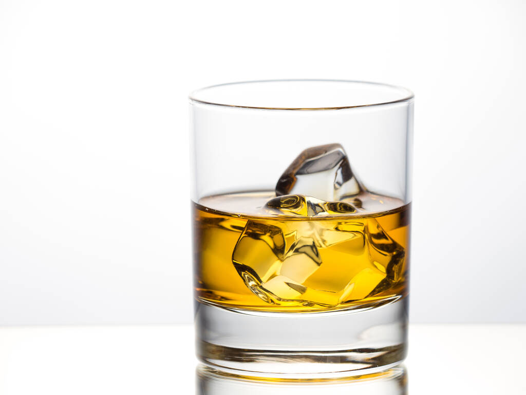 Whisky sobre las rocas sobre fondo blanco colocado sobre superficie reflectante - Foto, Imagen