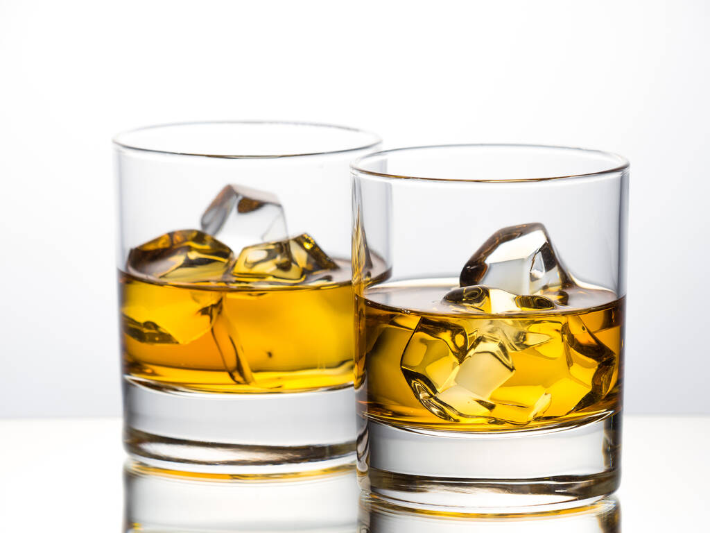 Whisky sobre las rocas sobre fondo blanco colocado sobre superficie reflectante - Foto, imagen