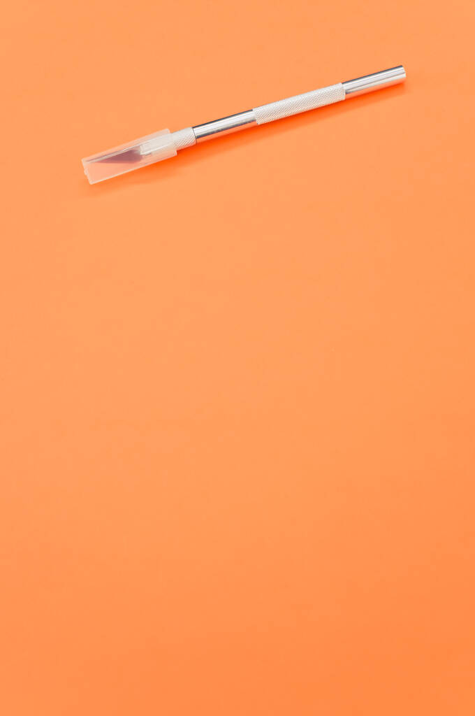 A vertical shot of metallic scalpel with cap isolated on orange background - Photo, Image