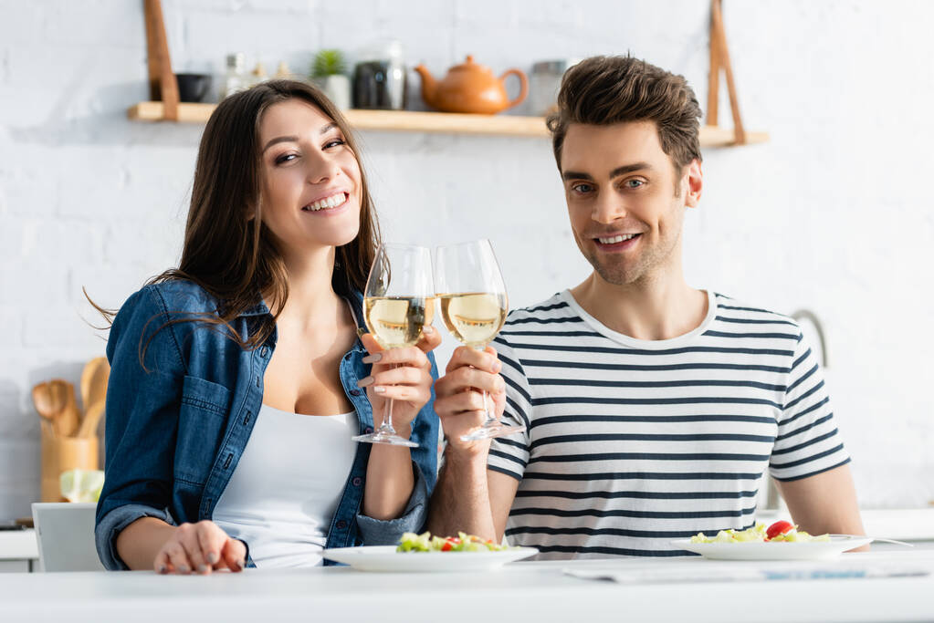 幸せなカップルキッチンでサラダとプレートの近くのワインのグラスをクリック  - 写真・画像