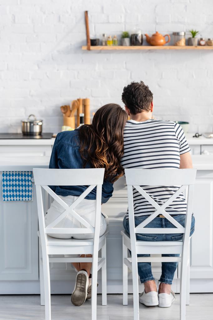 Вид сзади женщины, опирающейся на мужчину и сидящей на стуле на кухне  - Фото, изображение