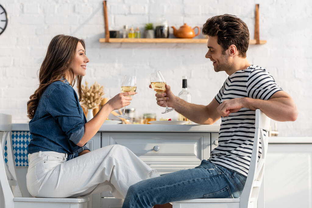 boční pohled na šťastný pár drží sklenice s vínem v kuchyni  - Fotografie, Obrázek