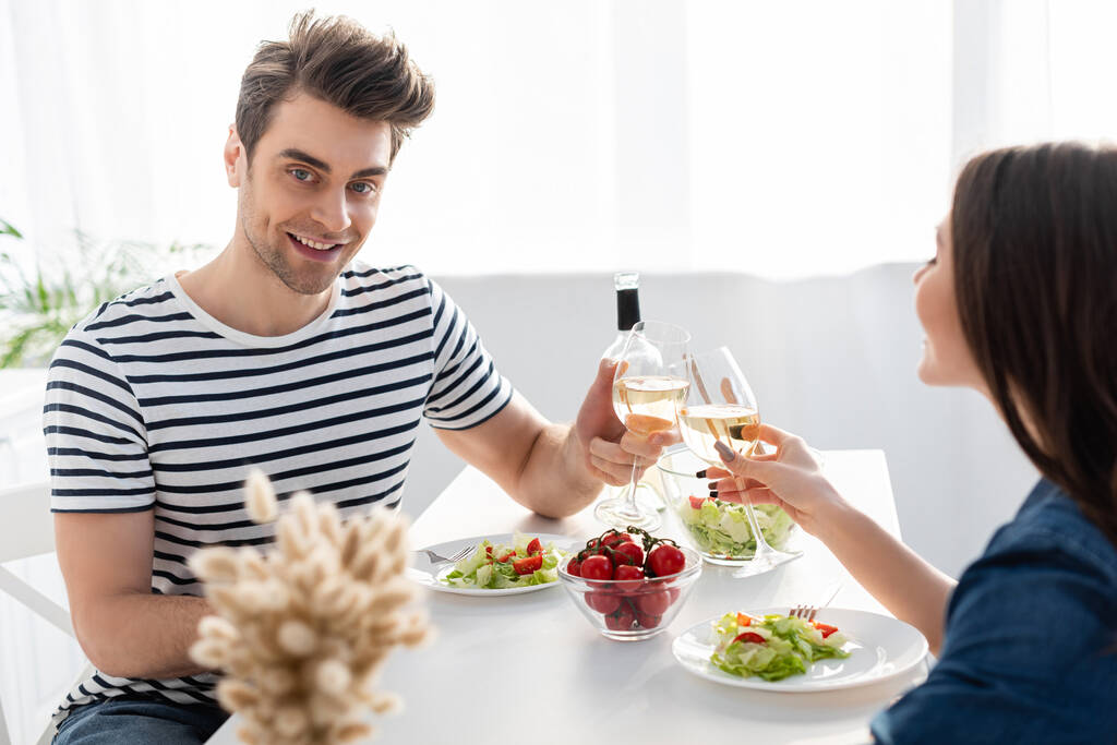 Χαρούμενος άνδρας και γυναίκα που κάνουν πρόποση με ποτήρια κρασιού κοντά στο μεσημεριανό γεύμα στο τραπέζι - Φωτογραφία, εικόνα