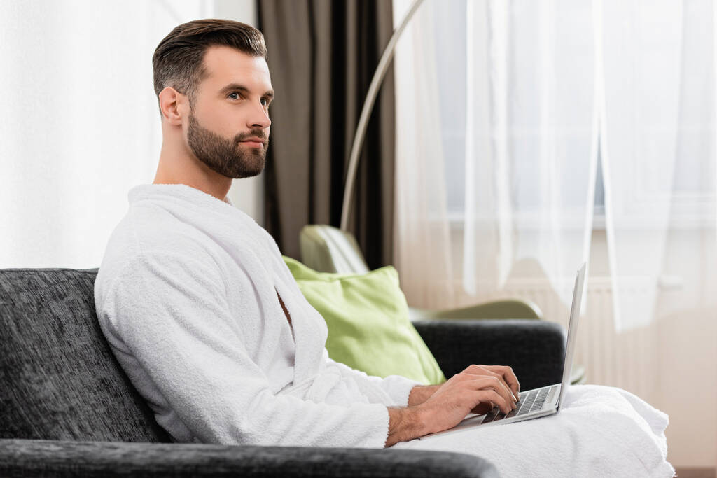 Freelancer em roupão branco usando laptop no quarto de hotel  - Foto, Imagem
