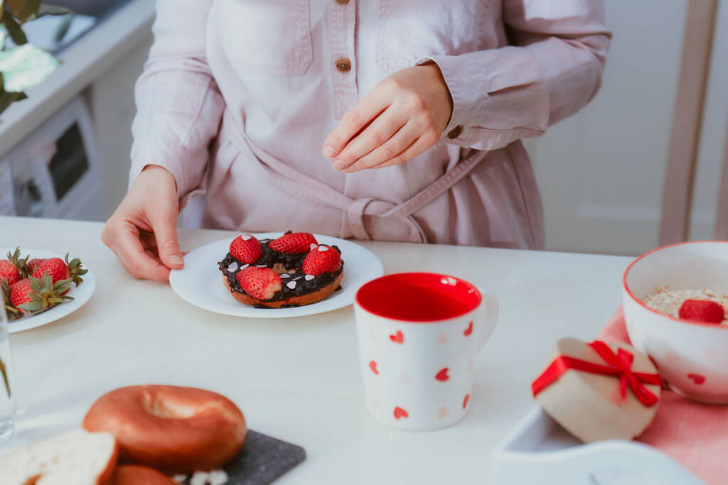 Mulher decorando bagel doce com geléia com morangos e doces em forma de coração. Preparando café da manhã surpresa para o amante no dia dos namorados. Ideias de comida festiva simples. Espaço de cópia - Foto, Imagem