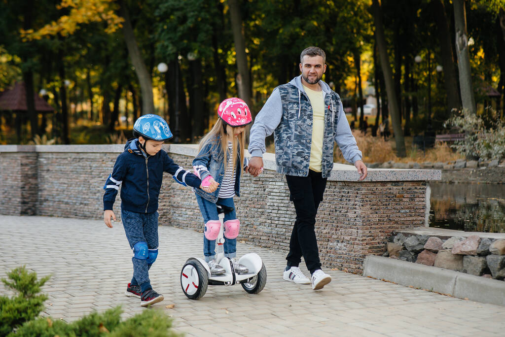 Een vader helpt en leert zijn jonge kinderen om tijdens zonsondergang op een Segway in het Park te rijden. Familie vakantie in het park. - Foto, afbeelding